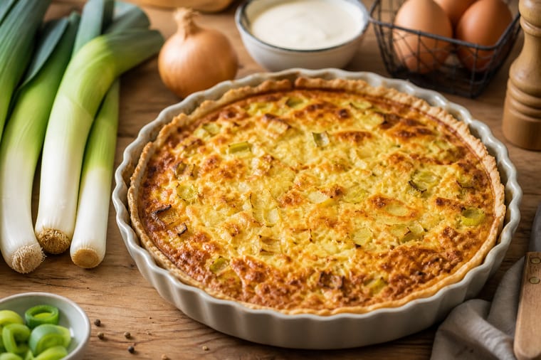 Quiche aux poireaux dorée servie sur une table avec des poireaux frais